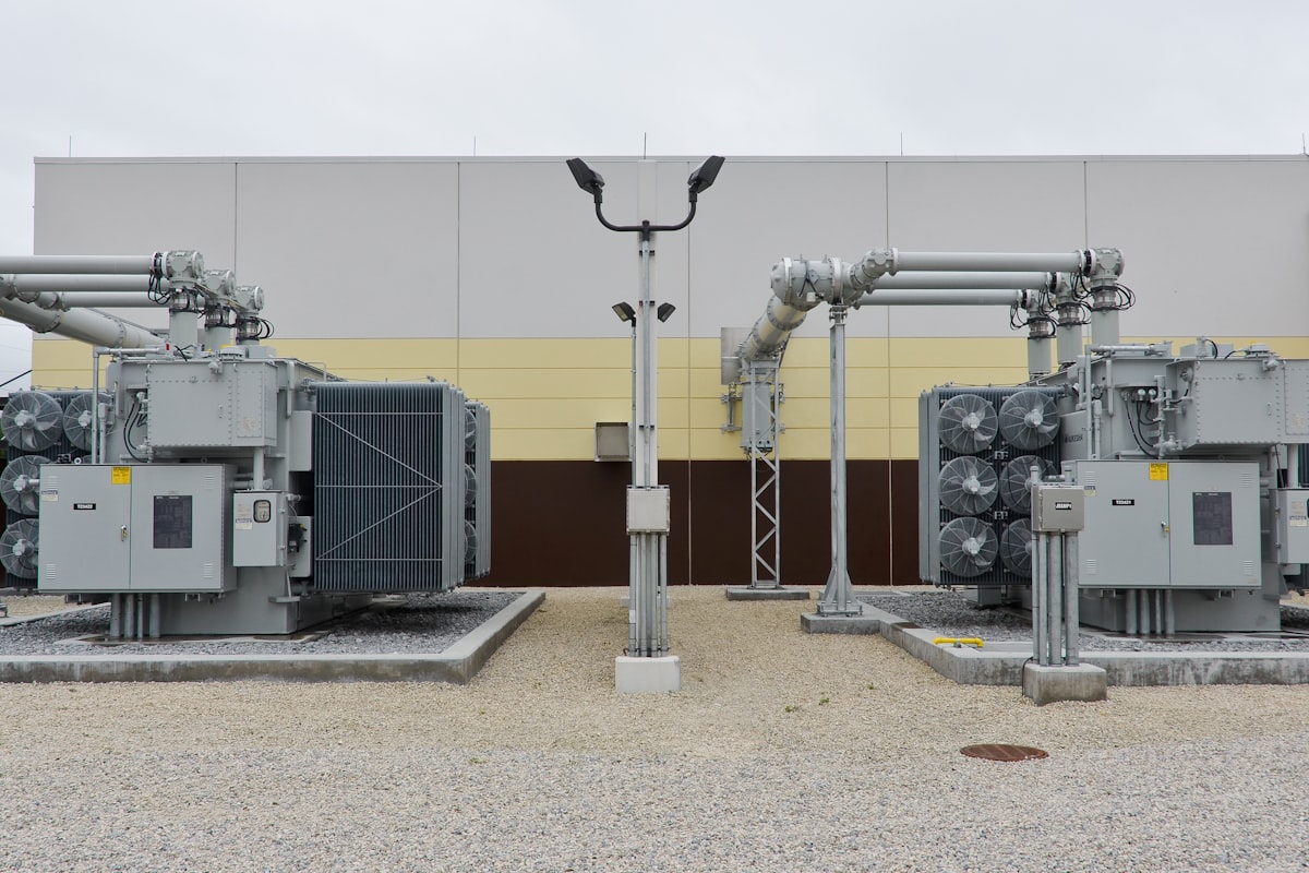 A modern substation with transformers and grey tubular gas-insulated bus ducts outside a GIS hall - the gas-insulated infrastructure whose SF6-or-alternative gas choice Pakistani utilities now plan around