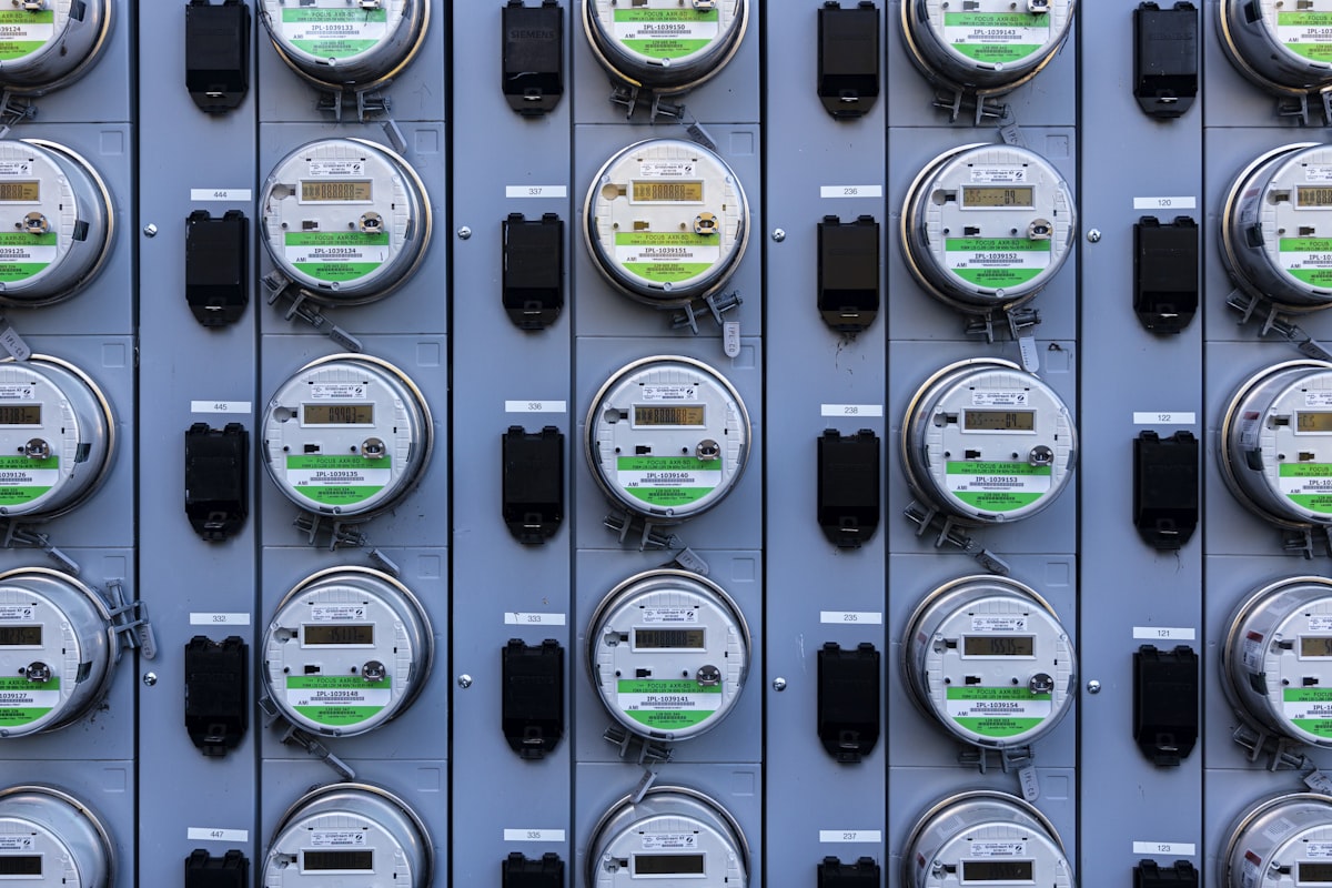 A dense array of modern digital electricity meters with LCD displays - the multi-point metering that an industrial energy-management system uses to allocate consumption line by line for ISO 50001 monitoring