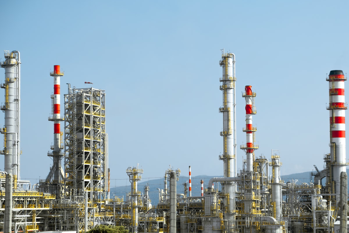 Industrial refinery with red and white process piping — the kind of hazardous-area installation where ATEX Zone 1 and Zone 2 explosion-proof enclosures, junction boxes, and control stations must be specified per IEC 60079-0 and IEC 60079-14
