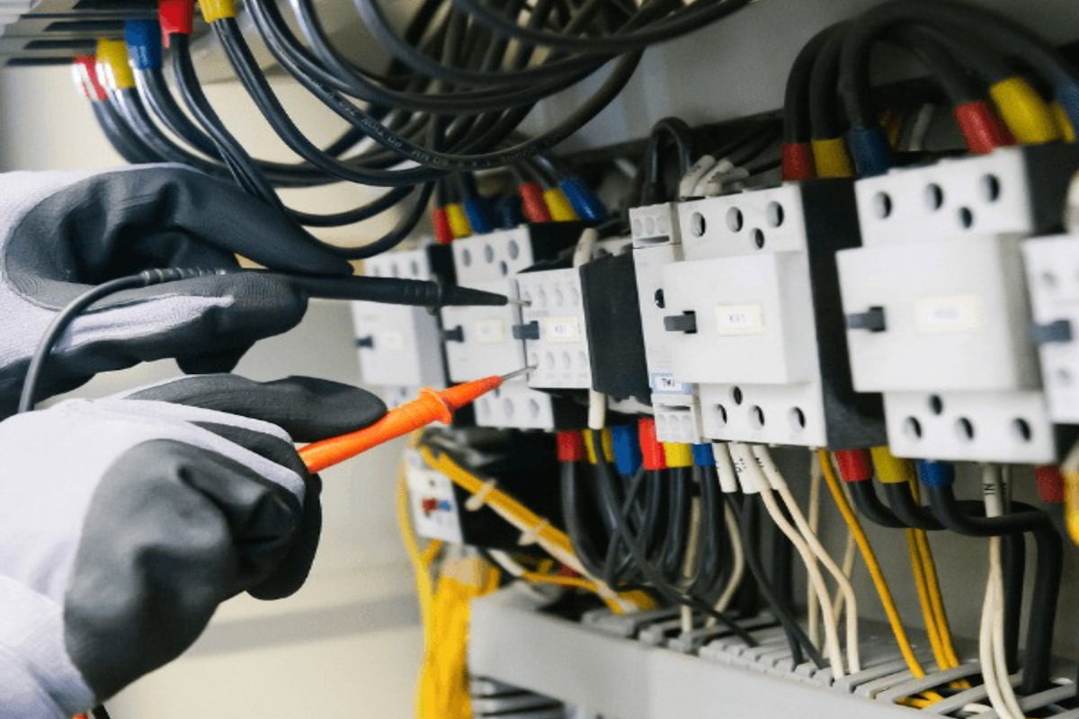Electrician testing an electrical panel with a multimeter inside a control cabinet — the kind of measurement chain where current transformer and energy meter accuracy classes determine billing integrity